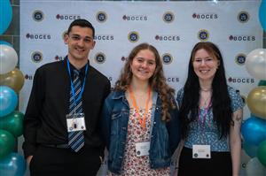 A group of 3 students in front of a backdrop posing for a photo. 