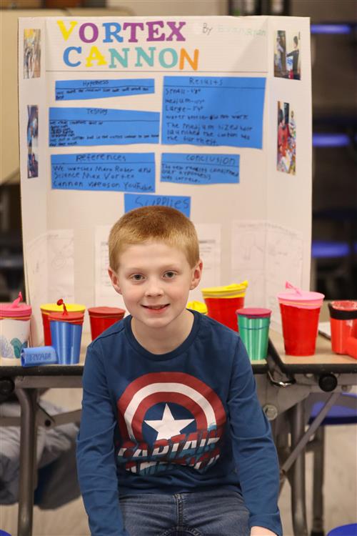 Boy sitting in front of his display at science fair.